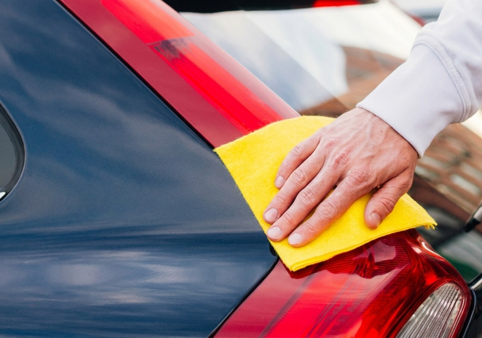 Hand working wax along a red rear quarter panel with a folded yellow microfiber, taillight just below