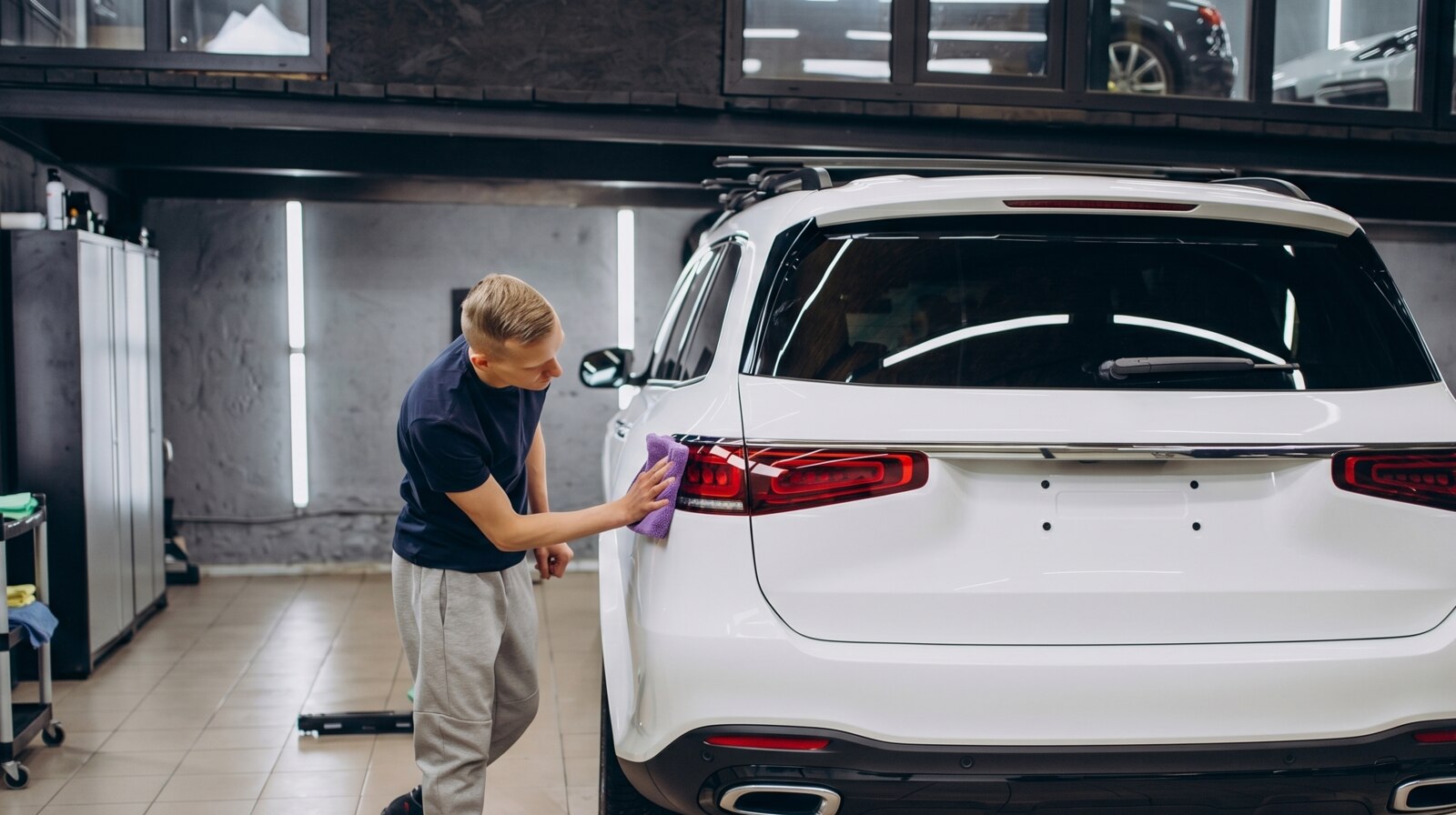 Detailer working the rear panel of a white SUV with a microfiber pad inside a clean detail shop
