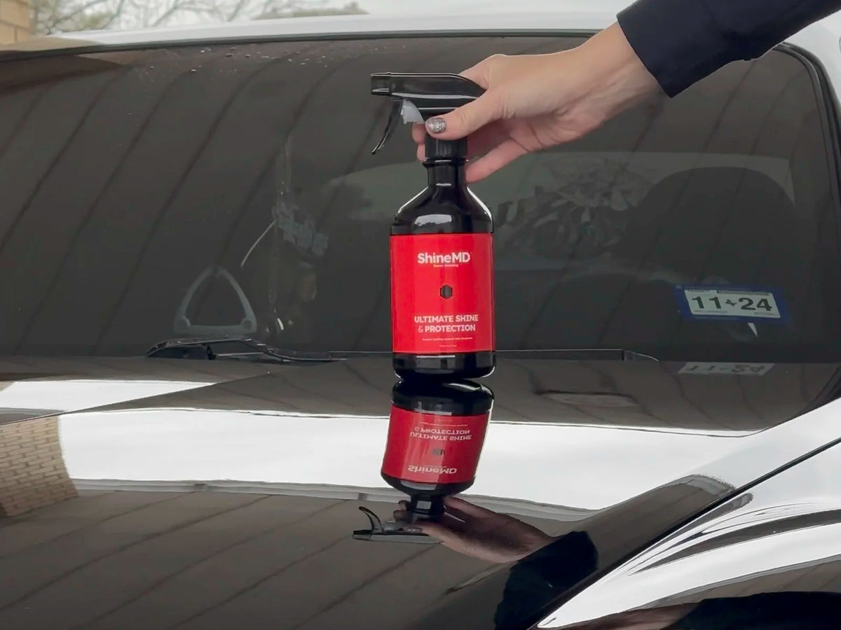 Hand holding the ShineMD bottle over the black hood of an RX-8, headlight curve reflected in the paint