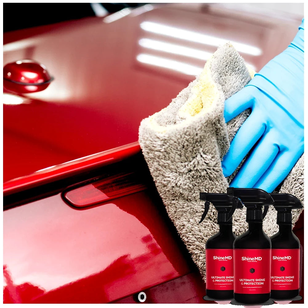 Macro composition: three ShineMD bottles and a microfiber towel resting on a deep glossy red car hood &mdash; the full applicator kit