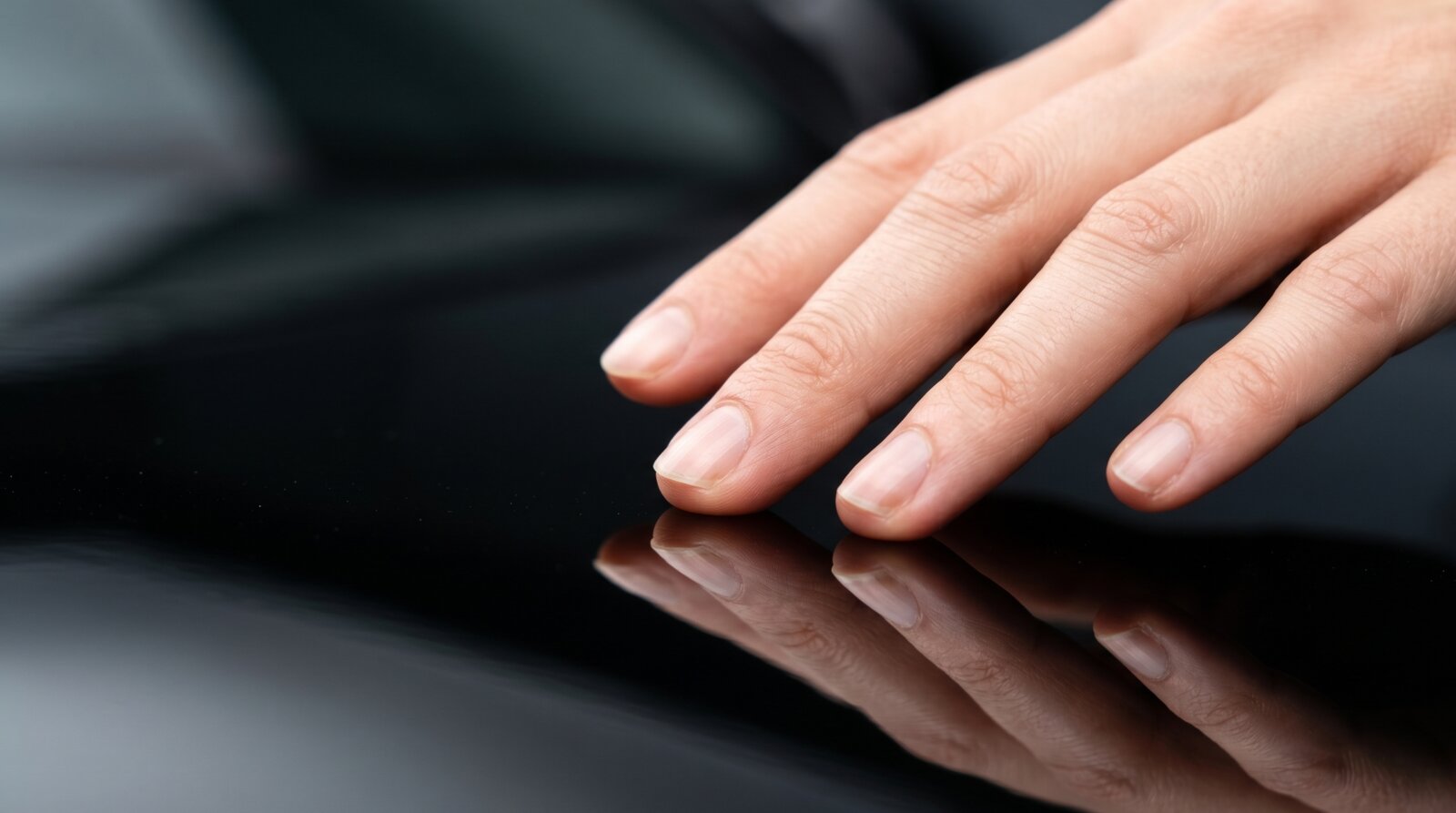 Macro of bare fingertips gliding across a freshly-coated deep glossy black car hood, reflection of the fingertips visible in the paint