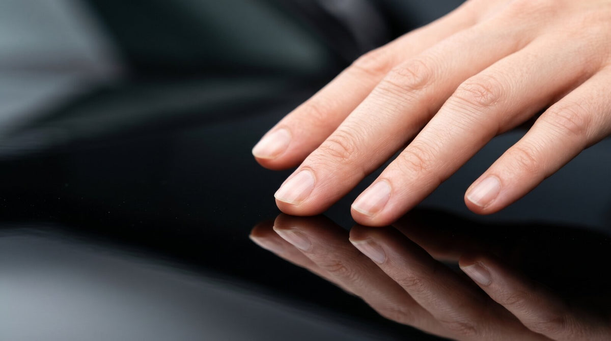Fingertips gliding across a freshly coated black panel, the hand mirrored in the gloss